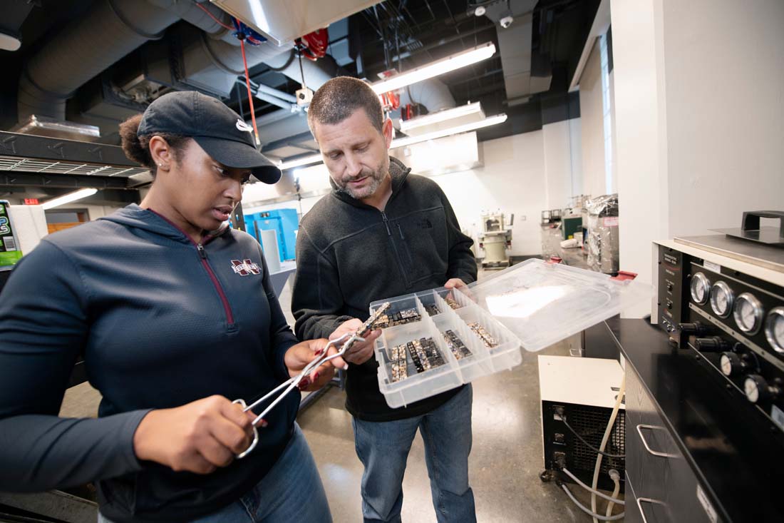 A student uses tweezers to pick a part from a tray held by a faculty member in a civil engineering lab